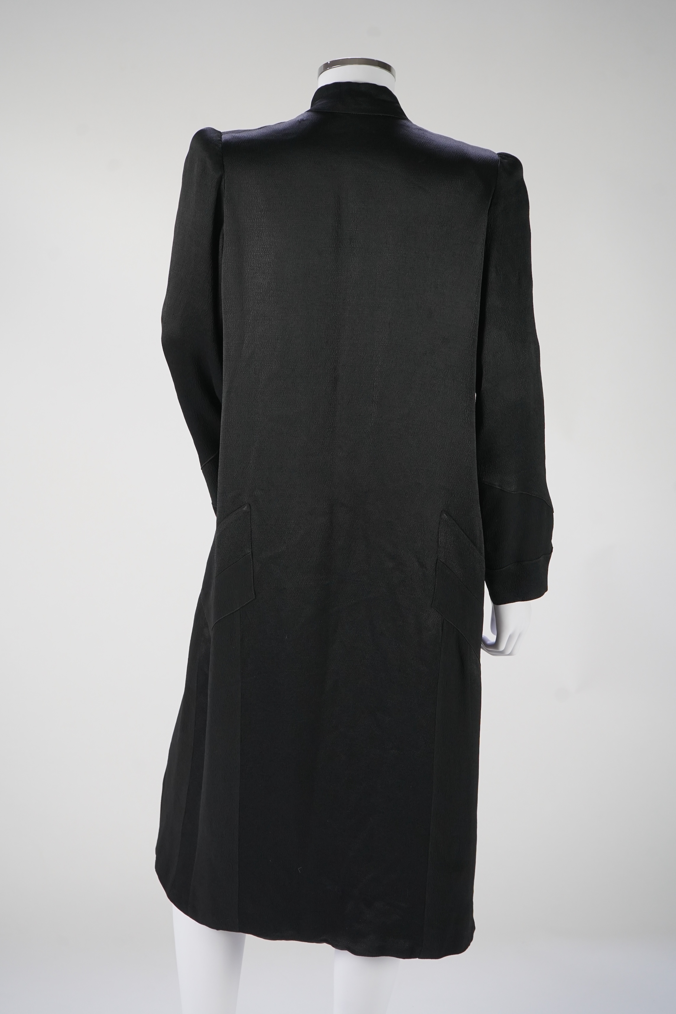 A 1930's black satin evening coat, with small collar and covered buttons to the front. Decorated with chevron motifs at side and lower sleeve detailing, front under arm width 19 inches, length back: top of collar to bott